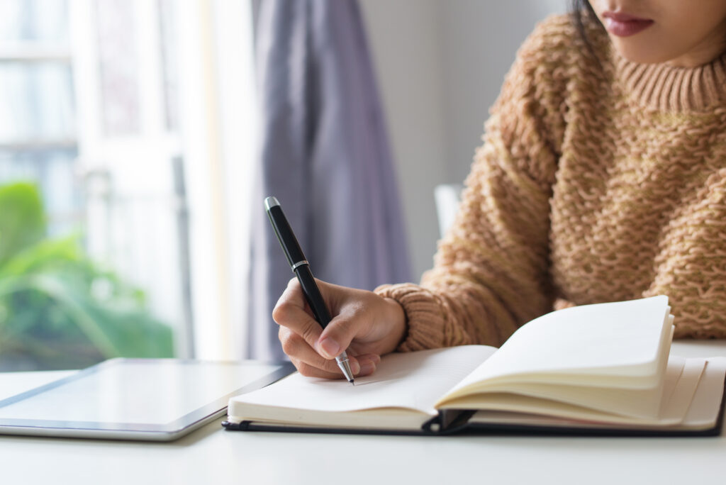 Close-up of pensive woman writing out ideas in diary. Busy woman sitting at table and making notes. Timetable concept